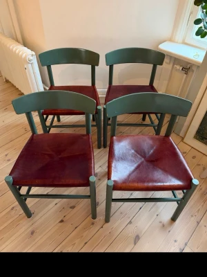 Fyra gröna stolar med lädersits - Säljer fyra stilrena stolar med mörkgröna träramar och sitsar i mörkbrunt läder. Stolarna har en klassisk design med bred ryggbräda och raka ben. Perfekta till köket eller matplatsen för dig som gillar retrovibbar och snygga materialval.