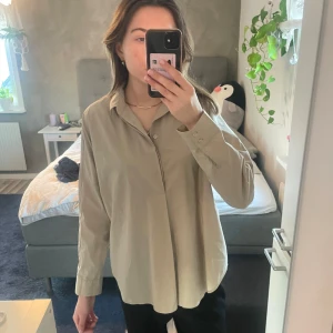 skjorta - Snygg beige skjorta med långa ärmar och klassisk krage. Perfekt för en stilren look. Skjortan har en avslappnad passform och knappar framtill.