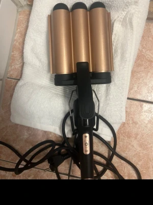 Trippelt våffeljärn för hår, svart/guld - Säljer ett trippelt våffeljärn för hår i svart och guld med sladd och kontrollknappar för temperatur. Perfekt för att skapa stora vågor i håret. Handtaget är svart och värmeplattorna har en snygg metallisk finish.