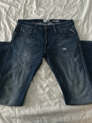 Blå Replay anbass jeans - Snygga blå jeans från Replay med klassisk femficksdesign och diskreta slitningar framtill. Jeansen har raka ben och detaljerade bakfickor samt läderpatch med logga bak i midjan. Tillverkade i denim med en cool tvättad look. Näst in till helt oanvända, användes 2-3 gånger då jag provade dem. Storlek W36 L34. Nypris 1899. Bara att skriva vid frågor!
