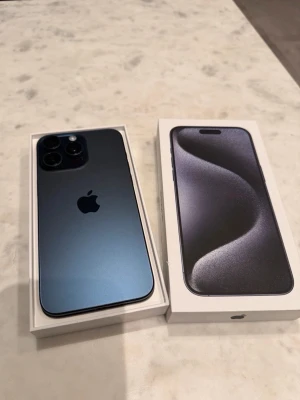 Svart Apple iPhone 15 Pro max - Snygg  iPhone 15 Pro med elegant matt finish och rundade kanter. Telefonen har tre kameror på baksidan och levereras i originalförpackning. Tillverkad i tåligt material med stilren design och Apples ikoniska logga på baksidan.