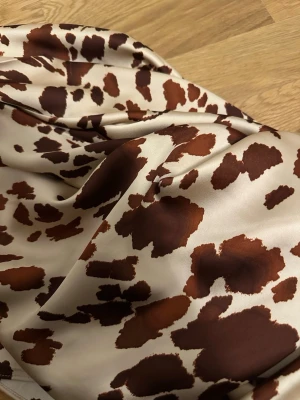 Långkjol stl xs - Snygg långkjol i glansigt satinmaterial i bruna och beige toner. Kjolen har en rak och elegant passform som faller snyggt längs benen. Perfekt för dig som vill sticka ut med ett djurmönstrat plagg.