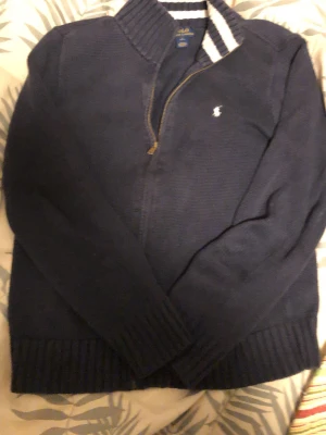 14-16 Marinblå stickad kofta Polo Ralph Lauren  - Säljer en marinblå stickad kofta från Polo Ralph Lauren med halv dragkedja och ribbade muddar. Den är knappt använd. Koftan passar dig mellan 160-173. Pris kan diskuteras. Svarar på allt.