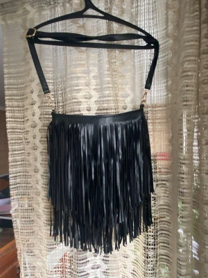 Svart handväska med fransar - Söt svart handväska med långa fransar och justerbar axelrem i veganläder. Själva väskan är 31x31 cm men fransarna är längre.