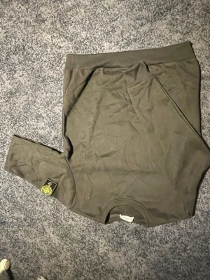  Stone Island sweatshirt, svart Stone Island Hoddie  - Säljer en svart sweatshirt från Stone Island med den klassiska logotypen på vänster ärm. Ljuset är lite konstigt, vilket gör att den ser grön ut. Den är svart. Perfekt för dig som gillar streetwear och vill ha en clean look.