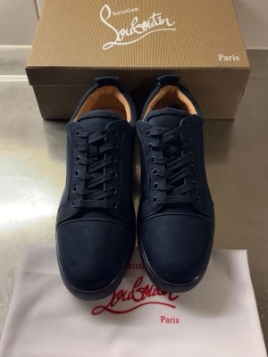 Mörkblå sneakers från Louboutin - Snygga mörkblå sneakers från Christian Louboutin i mocka med klassisk låg siluett. Skorna har matchande mörkblå snörning, diskret sömnad och beige innersula. Perfekta för dig som vill ha en stilren och exklusiv look.