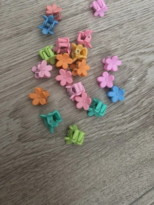 Färgglada blomformade hårklämmor - Säljer 20 små hårklämmor i plast med blommotiv i flera färger som rosa, orange, blå, grön och gul. Perfekta för att skapa söta frisyrer eller piffa till din look. Klämmorna har en enkel klämfunktion och är lätta att använda.❣️