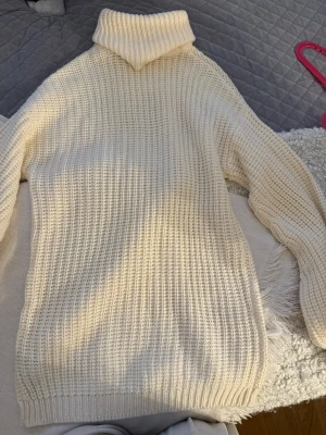 Krämvit polotröja i grovstickat - Säljer en krämvit polotröja i grovstickat material med ribbade muddar och hög krage. Tröjan har lång ärm och en avslappnad passform, perfekt för kalla dagar. Materialet känns mjukt och mysigt mot huden.