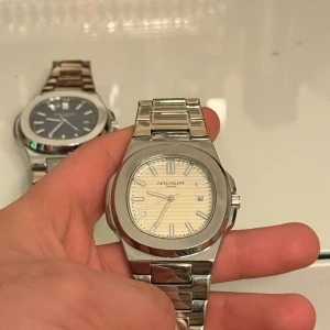 Herrklocka - Stilren med silverfärgat armband och boett i rostfritt stål. Urtavlan är ljus med subtila horisontella ränder och silverdetaljer. Klassisk design som sticker ut med sin eleganta form och exklusiva känsla.