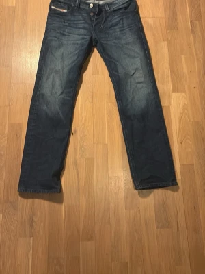 Mörkblå raka jeans från Diesel - Snygga mörkblå jeans från Diesel med raka ben och klassisk femficksmodell. Jeansen har en knappgylf och diskreta slitningar för en cool look. Tillverkade i denim med en autentisk tvätt som ger en avslappnad känsla. 32W 30L