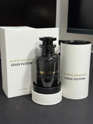 Louis Vuitton Ombre Nomade Eau de parfum 100ml - Exklusiv parfym från Louis Vuitton, Ombre Nomade, i en elegant mörk glasflaska med guldfärgad text. Flaskan rymmer 100 ml och kommer i en stilren vit förpackning med svart och guld detaljer. Lyxig design som verkligen sticker ut på parfymhyllan.