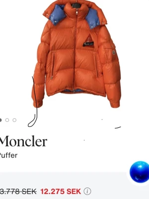 Orange pufferjacka Moncler Wilson - Orange pufferjacka Moncler Wilson med blått foder i huvan och detaljer som logotyp-patch på bröstet och en avtagbar huva.                  Originalpris 12 900kr, köpt i                     MONCLER BUTIKEN Birgerjarslgatan kvitto o allt går att ordna 