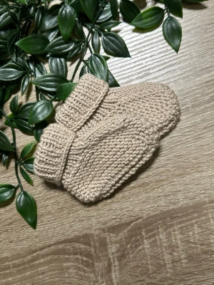 Beige stickade babytossor - Supersöta beige stickade babytossor med uppvikta muddar. Perfekta för att hålla små fötter varma under kyliga dagar. De är handgjorda i mjukt garn och har en enkel, klassisk design. Storlek nyfödd