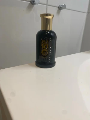 BOSS Bottled Elixir parfym 50 ml - Snygg parfymflaska från Hugo Boss, modell Bottled Elixir. Flaskan är svart med gulddetaljer och har en elegant, rundad form. Märket och namnet syns tydligt i guld på framsidan. Perfekt för dig som gillar exklusiva dofter och stilren design. 80% kvar