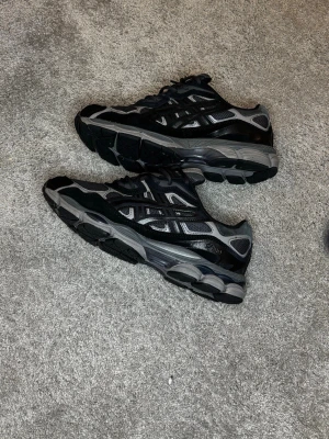 Svarta Asics Gel nyc storlek 44 - Säljer ett par svarta och grå Asics Gel nyc sneakers med mesh och syntetiska detaljer. Skorna har en chunky sula och klassisk Asics-logga på sidan. Perfekta för dig som gillar sportig och trendig stil. Storlek 44