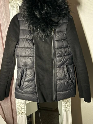 Svart pufferjacka med fuskpäls  - Svart pufferjacka från Lolita med fluffig fuskpäls runt kragen och insidan. Jackan har quiltade paneler, dragkedja framtill och två fickor. Ärmarna är släta med päls inuti. Perfekt för kalla dagar och riktigt snygg stil fick så många komplimanger när jag hade på mig den.✨😍