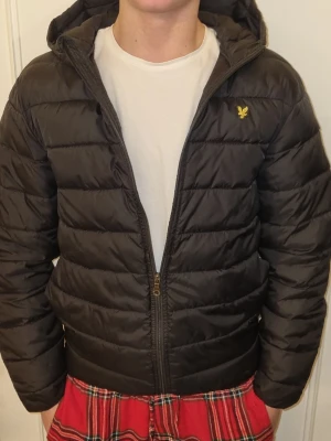 Svart pufferjacka från Lyle & Scott - Säljer en svart pufferjacka från Lyle & Scott med gul logga på bröstet. Storlek 12-13 år. Har sytt ihop den under högra armen men märks knappt. Hör av vi funderingar