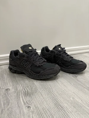 Svarta New Balance 2002R sneakers - Säljer ett par svarta New Balance 2002R sneakers med slitna detaljer och meshpaneler. Skorna har en chunky sula och klassisk N-logga på sidan. Skorna är köpta från Merch sweden finns även kvitto på det.