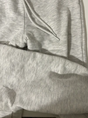 Ljusgrå mjukisbyxor med dragsko - Snygga ljusgrå mjukisbyxor med dragsko i midjan och resår vid bensluten. Tillverkade i mjukt och bekvämt material, perfekta för chill dagar. Klassisk passform och stilren look.