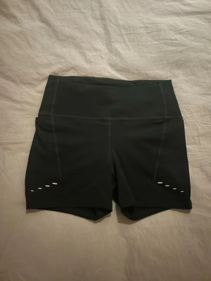 Svarta löparshorts från Nike - Snygga svarta löparshorts från Nike med reflekterande detaljer. Tillverkade i ett stretchigt funktionsmaterial som andas. Perfekta för träning och löpning, med liten ficka bak.