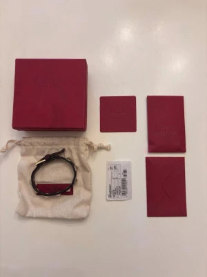 Valentino svart läderarmband nitar - Snyggt svart armband från Valentino i äkta läder med ikoniska pyramidformade silverfärgade nitar. Justerbart spänne och exklusiv känsla. Kommer med originalförpackning och tillbehör som dustbag och certifikat.