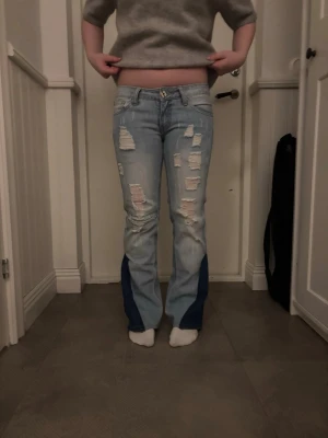 Unika coola jeans! 🍒🩵 - Säljer ett par lågmidjade  ljusblå bootcut jeans med slitningar och hål framtill samt mörkblå paneler nedtill på benen som jag har sytt dit.🩵🩵🩵