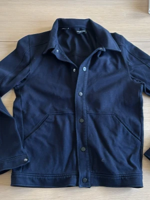 Marinblå overshirt från selected homme - Stilren svart overshirt från selected homme i kraftigt bomullstyg. Modellen har klassisk krage, tryckknappar framtill och två stora snedställda fickor. Perfekt lager-på-lager-plagg med enkel, modern look och raka linjer. utmärkt för våren.