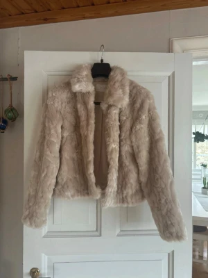 Beige pälsjacka från VILA - Säljer en fluffig och mjuk beige pälsjacka från VILA. Jackan har klassisk krage, knappar framtill och är helfodrad. Perfekt för dig som vill ha en trendig och varm look med lite lyxig känsla. Långärmad och i kortare modell.