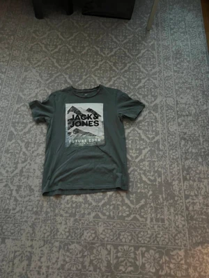 Grå Jack & Jones t-shirt med tryck - Säljer en grå t-shirt från Jack & Jones med stort grafiskt tryck framtill och texten 'Future Edit'. Klassisk rund hals och korta ärmar. Perfekt för dig som gillar streetwear och enkel stil.