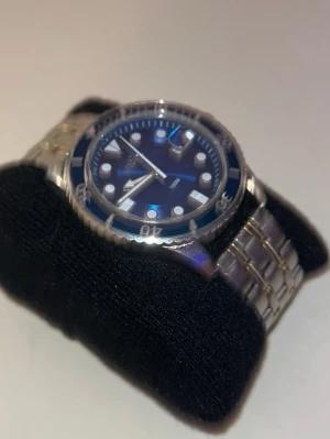 stilrena klocka - Säljer två snygga armbandsur med metallänk. Den ena har en blå urtavla med tydliga markeringar och vridbar ring, medan den andra har en lila urtavla med silverdetaljer och tachymeter. Perfekta accessoarer för dig som gillar klassisk stil.