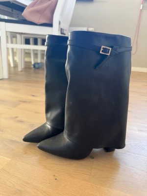 Svarta stövlar med klack - Snygga svarta stövlar med spetsig tå och bred klack. Dekorativt spänne upptill. De är använda, vilket man kan se fram på skon att den är har skavt lite.