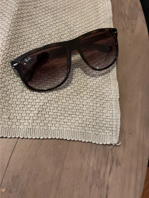 Svarta Ray-Ban Wayfarer solglasögon - Klassiska svarta boyfriend solglasögon från Ray-Ban med mörka glas och stilren design. Bågarna är i plast och har Ray-Ban-loggan på sidan. Perfekta för soliga dagar och ger en tidlös look.