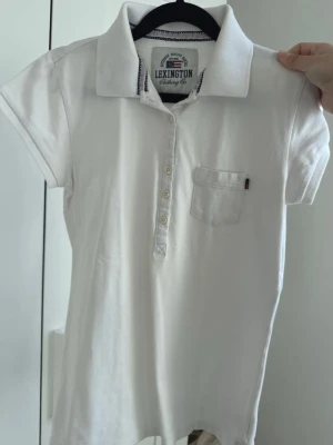 Vit pikétröja från Lexington - Klassisk vit pikétröja från Lexington med korta ärmar, krage och knappar framtill. 