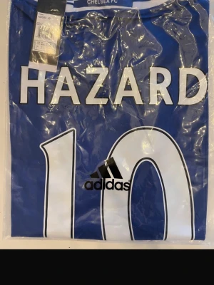 Chelsea FC Hazard matchtröja blå 2017 - Helt ny! Snygg blå Chelsea FC matchtröja från Adidas med HAZARD och nummer 10 tryckt på ryggen. Klassisk fotbollströja med vita detaljer och klubbnamn i nacken. Perfekt för dig som älskar fotboll och vill visa ditt stöd för laget.