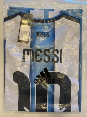 Argentina Messi matchtröja 2026 vm - Helt ny! MESSI 10. Säljer en snygg Argentina matchtröja från Adidas med Messi-tryck på ryggen. Tröjan har klassiska blå och vita ränder, svart Adidas-logga och är tillverkad i lätt och ventilerande material med AEROREADY-teknologi. Perfekt för fotbollsfans!