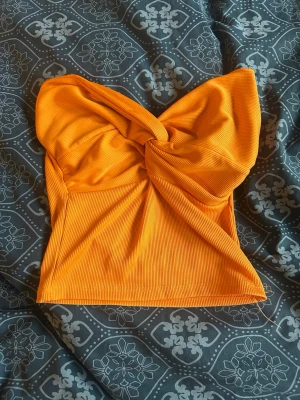 Orange ribbad bandeau topp - Trendig orange bandeau topp med twistad detalj framtill och ribbad struktur. Toppens material är stretchigt och sitter snyggt på kroppen. Passar xs-s, den är köpt i ungern på en loppis så det står inget om vart den är ifrån eller sånt. Skriv för mer info💕