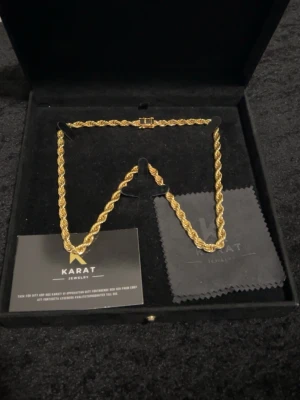 Guldfärgat tvinnat halsband Karat - Snyggt guldfärgat halsband från Karat Jewelry med tvinnad kedja som ger en exklusiv look. Halsbandet har en klassisk låsning och levereras i en elegant svart ask. Perfekt accessoar för att lyfta din outfit.18k