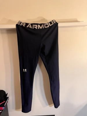 Svarta/blå leggings L - Snygga svarta/blå leggings från Under Armour med bred resår i midjan.Stretchigt material som sitter tight och är perfekt för träning. använd få gånger