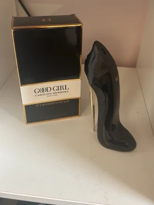 Good Girl parfym från Carolina Herrera 80ml - Snygg parfymflaska från Carolina Herrera i form av en svart högklackad sko med gulddetaljer. Doften heter Good Girl och kommer i en lyxig svart och guld förpackning. Perfekt för dig som gillar unika och eleganta parfymer.