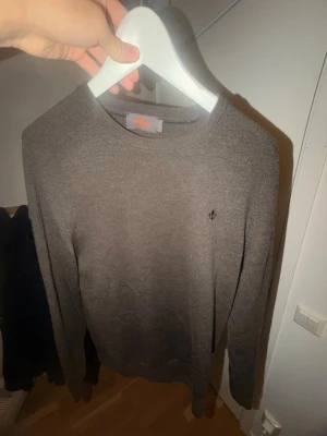 Brun stickad tröja med logga - Mjuk och stilren brun stickad tröja med rund hals och diskret broderad logga på bröstet. Tröjan har långa ärmar och ribbade muddar vid ärmslut och nederkant. Perfekt för lager på lager och enkel att matcha. Den är använd under 5 gånger