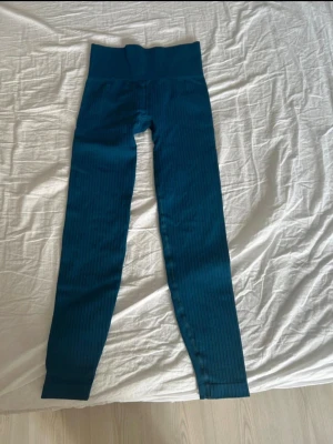 Mörkblå ribbade leggings - Säljer ett par mörkblå leggings med ribbad struktur och hög midja. De är stretchiga och har en smickrande passform som sitter tajt längs benen. Perfekta för en trendig och bekväm look.
