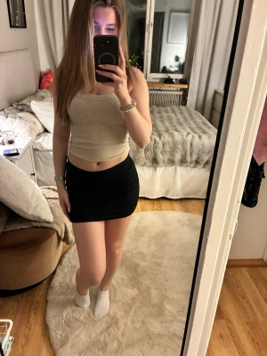 Svart tight kortkjol - Säljer en svart tight kortkjol som sitter snyggt och markerar midjan. Kjolen har enkel design utan mönster eller detaljer och passar perfekt till en croppad topp. Materialet känns mjukt och stretchigt, troligen polyester eller bomull.