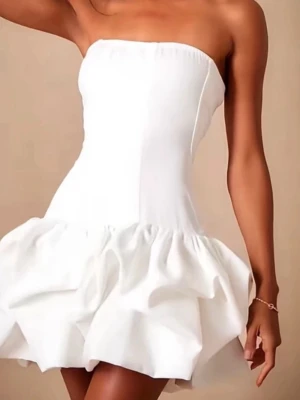 Vit axelbandslös kort klänning - Trendig vit axelbandslös kort klänning med volangig kjol och figurnära passform upptill. Perfekt för dig som vill sticka ut med en stilren och modern look. Tillverkad i ett mjukt material som ger en snygg siluett.
