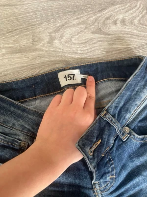 Blå bootcut jeans från 157 - Säljer ett par klassiska blå bootcut jeans från 157 med snygg tvätt och kontrastsömmar. Jeansen har fem fickor och normalhög midja. Perfekta för dig som gillar en avslappnad men trendig stil.