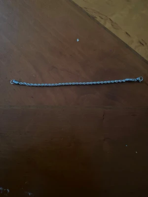 Tunt silverfärgat kedjearmband - Säljer ett stilrent och tunt armband i silverfärg med tvinnad kedja och enkel karbinhake. Perfekt för dig som gillar minimalistiska accessoarer och vill ha något diskret men ändå snyggt runt handleden. Passar till många olika stilar och är lätt att matcha.