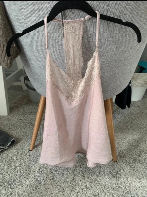 Ljusrosa spetsnattlinne med racerback - Säljer ett ljusrosa nattlinne med tunna axelband och vacker spetsdetalj både fram och bak. Nattlinnet har en racerback-design med bred spetspanel och ett mjukt, lätt material som känns skönt mot huden. Perfekt för en avslappnad kväll hemma.
