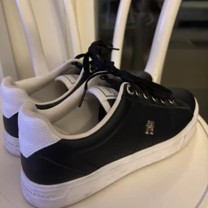 Svarta Tommy Hilfiger sneakers - Snygga svarta sneakers från Tommy Hilfiger med vita detaljer och metallfärgade öglor.