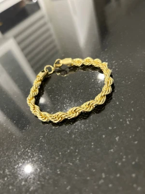 Cordell Armband 7mm - Snyggt armband i guldfärgad metall med tvinnad design. Armbandet har en klassisk karbinhake och passar perfekt för dig som gillar stilrena accessoarer med lite extra edge. Perfekt att bära ensam eller att matcha med andra smycken.