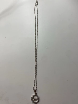 Silverfärgat halsband med pärlor - Snyggt halsband i silverfärg med en rund berlock dekorerad med små vita pärlor. Kedjan är tunn och elegant, perfekt för att ge en stilren touch till din outfit. Berlocken har en modern design med pärldetaljer som gör halsbandet extra unikt.