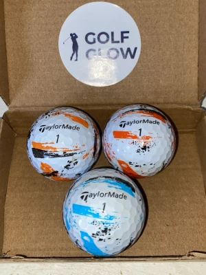 Taylormade speedsoft ink 3-pack - Tre vita golfbollar från TaylorMade med unika färgstänk i orange, blått och svart. Bollarna har nummer 1 tryckt på sig och levereras i en enkel kartong med GOLF GLOW-logga på insidan av locket. Perfekta för dig som vill sticka ut på golfbanan.